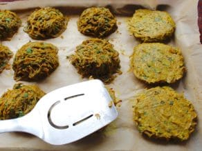Flipping and flattening potato pancakes with a stainless steel spatula that's on a baking sheet and tray