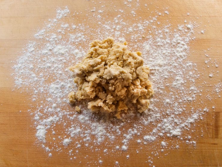 A mound of raw dough sits on a wooden surface, surrounded by scattered white flour.