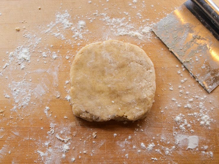 A ball of dough rests on a floured wooden surface next to a metal dough scraper.