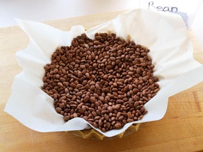 A pie crust lined with parchment paper is filled with dry beans, resting on a wooden surface.