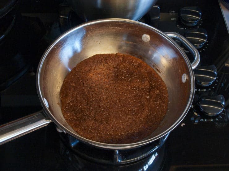 A silver pan on a black stovetop, filled with brown, bubbling sauce mixture of brown sugar and butter.