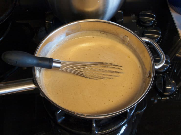 A saucepan on a stove with thicken mixture of brown sugar and butter sauce being whisked.