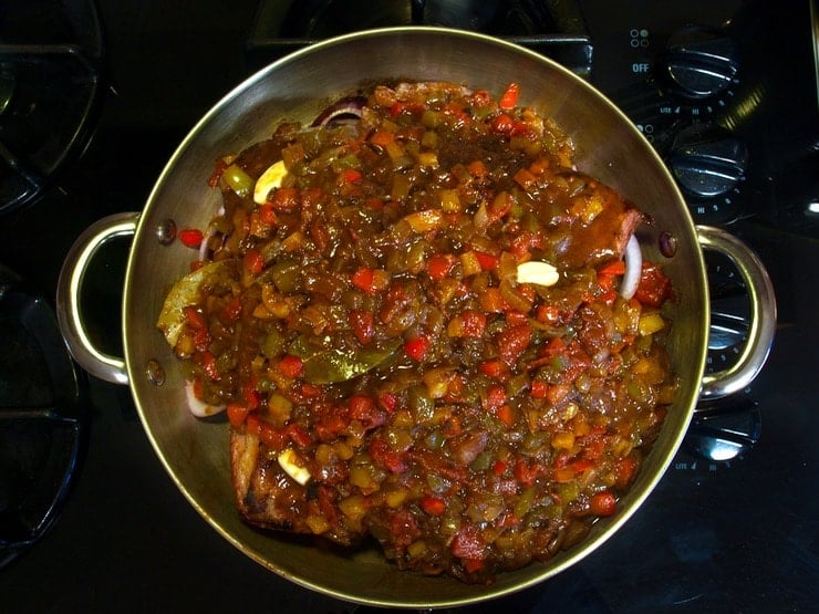 Brisket and onions topped with sauce in pan on stovetop.