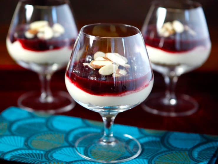 Three glasses of Cherry Cheesecake Shooters topped with almonds and berries, a delightful dessert