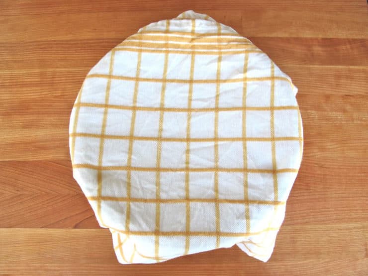 Challah dough in a bowl covered with a damp towel.