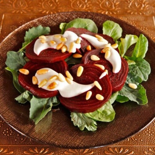 Roasted Beets with Tahini and Pine Nuts served over greens on a plate.