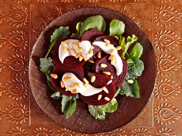 Roasted Beets with Tahini and Pine Nuts served over greens on a plate.