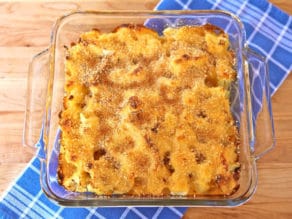 Close-up of roasted cauliflower gratin in a clear rectangular glass container, placed on a blue checkered cloth.