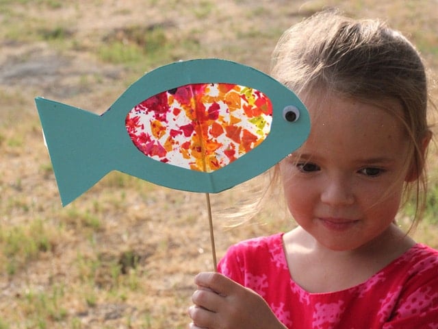 A small girl holding a stained glass fish art work