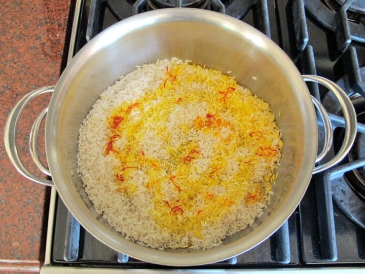 Saffron water added to cooked rice in a saucepan.