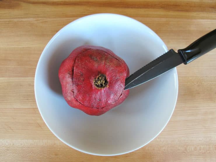Carefully cutting the top end off a pomegranate.