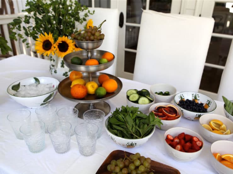 A table full of fruits in a bowl, a fruit stand, and glasses.