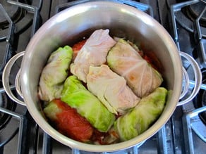 Layering cabbage rolls and tomato sauce in a pot.
