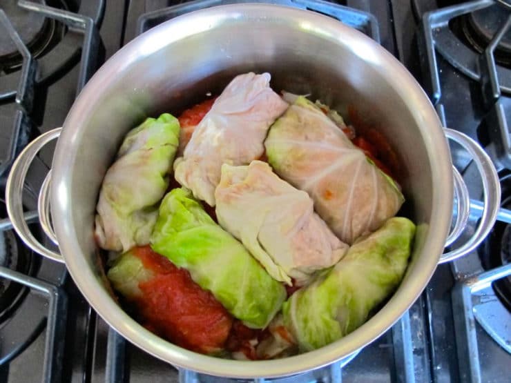 Layering cabbage rolls and tomato sauce in a pot.