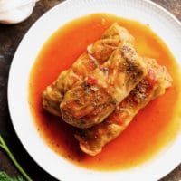 Three stuffed cabbage leaves - holishkes on a plate with sauce, fresh dill and garlic on the side.