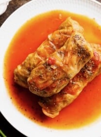 Three stuffed cabbage leaves - holishkes on a plate with sauce, fresh dill and garlic on the side.