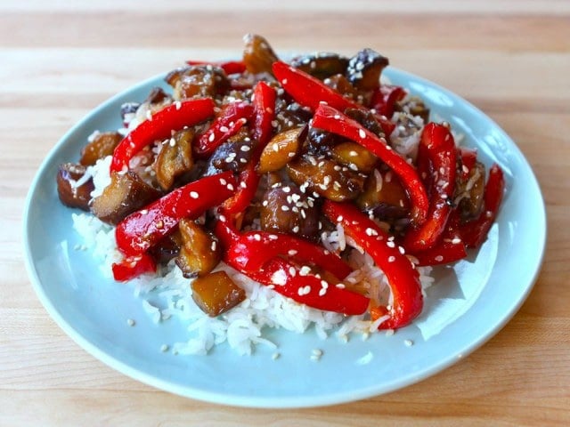 A close-up view of delectable Sweet and Sour Eggplant, beautifully presented on a round plate, set atop a rustic wooden table.