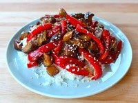 A close-up view of delectable Sweet and Sour Eggplant, beautifully presented on a round plate, set atop a rustic wooden table.