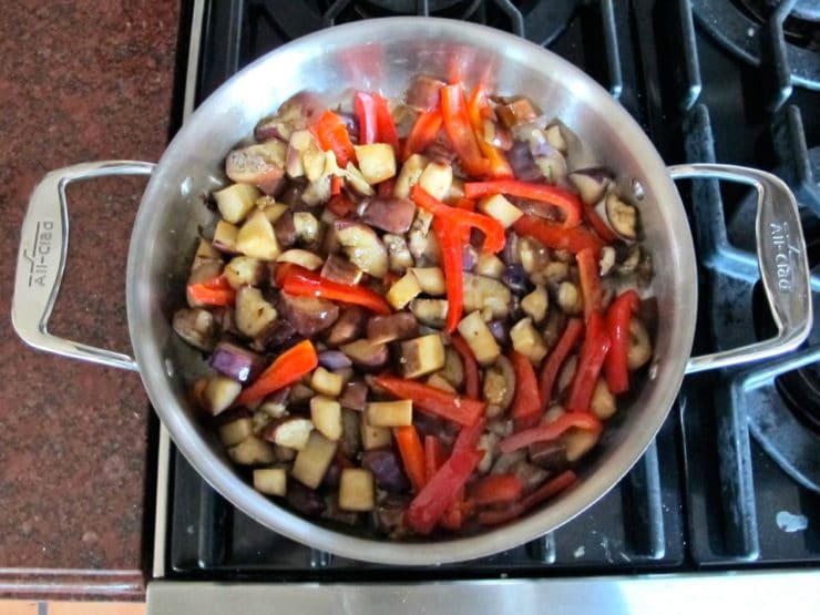 Sliced red bell peppers added to eggplant in skillet.