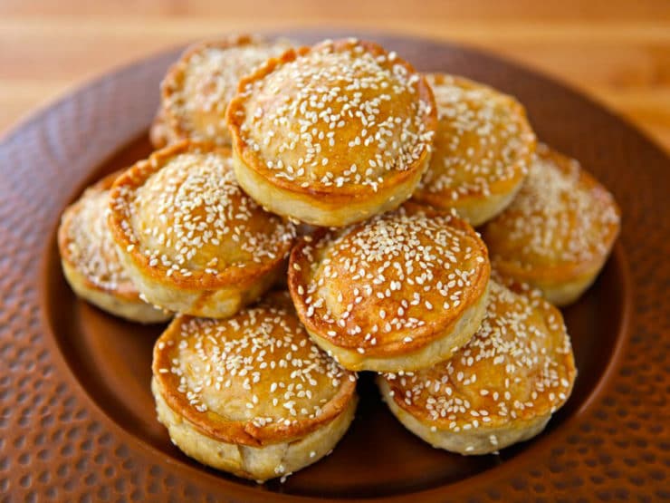 Sephardic Meat Hand Pies sprinkled with sesame seeds stock on top of each other served in a fancy brown plate.
