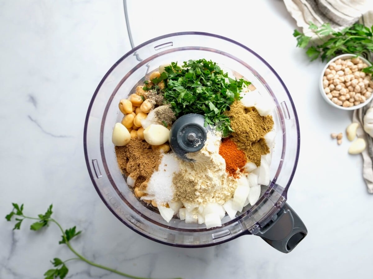 Horizontal overhead image of a food processor bowl filled with falafel ingredients.