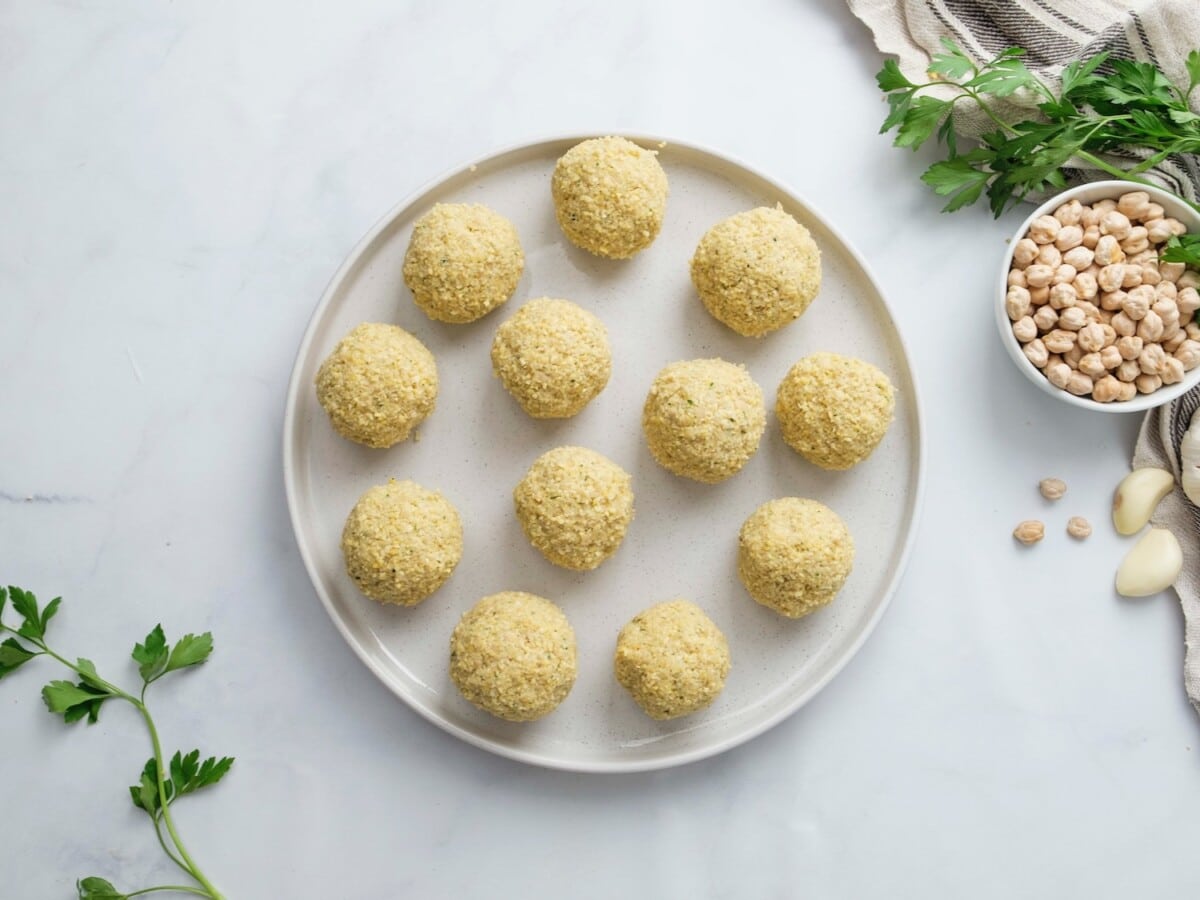 Horizontal overhead image of a white plain containing uncooked falafel balls.