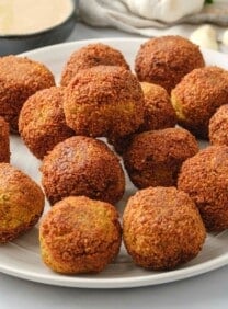 A white plate filled with falafel balls next to a bowl of tahini sauce.