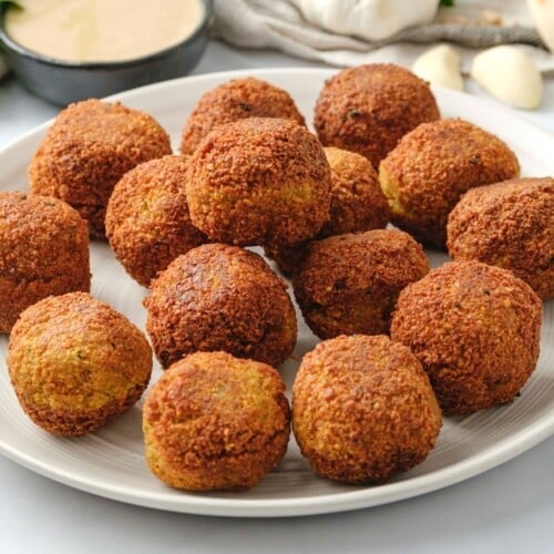 A white plate filled with falafel balls next to a bowl of tahini sauce.