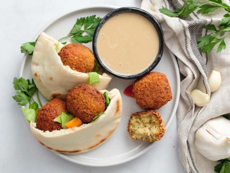 A plate containing a pita pocket filled with falafel next to a small black dish of tahini sauce.
