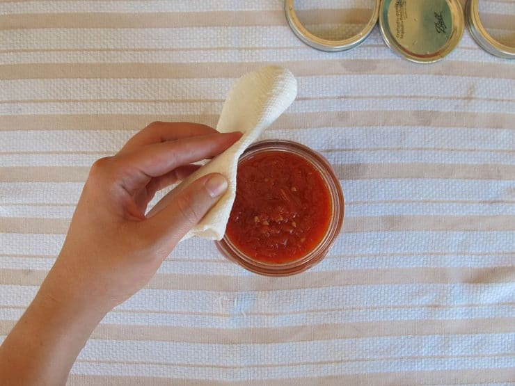 Cleaning the rims of canning jars with a towel.