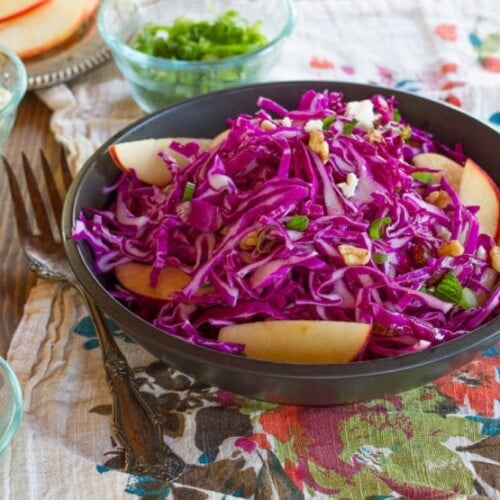Red Cabbage Apple Salad with Blue Cheese in a blue bowl on a table next to a fork.