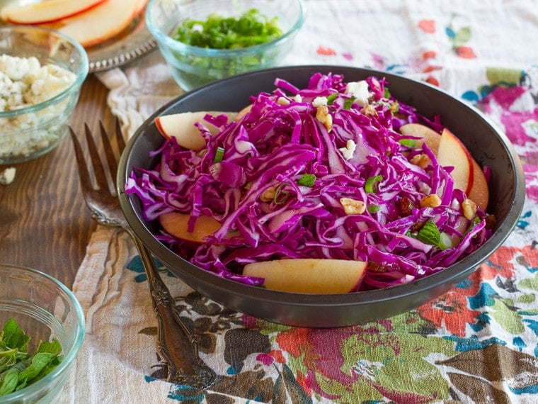Red Cabbage Apple Salad with Blue Cheese in a blue bowl on a table next to a fork.