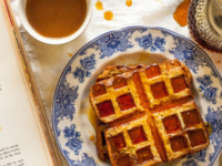 Close-up of two Bread and Butter Waffles soaked on syrup served on a fancy plate with coffee on the side