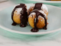 Buñuelos with Warm Chocolate Sauce Pinterest Pin - Golden-brown Buñuelos on a white plate, topped with rich warm chocolate sauce and a dusting of powdered sugar, creating a warm, indulgent vibe.