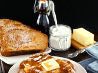 Challah French toast topped with butter and syrup on a white plate
