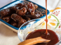 Dates served on a square-shaped bowl and date honey syrup pouring from a glass pitcher to a glass bowl with wooden spoon,