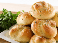 Garlic Knots served on a squared shaped white plate with garlic cloves and parsley on the side