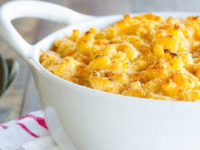 A white baking dish filled with macaroni and cheese on a red and white towel atop a wooden background.