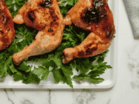 Golden-brown honey garlic chicken garnished with fresh parsley at the bottom, presented on a white plate. A vibrant lemon wedge on the side.