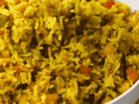 Horizontal close up - spoon digging into fluffy yellow vegetable rice with pieces of eggplant and carrot.