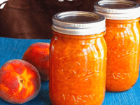Close-up of Two jars of Peach Saffron Preserves and peaches on a blue tablecloth, showcasing the delicious peach jam