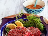 Red Rice and Beet Cakes with Honey Mustard served on a blue plate with two slices of lemon wedges and a herb with a dipping sauce on the back