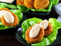 Sriracha Seared Salmon Cakes Pinterest Pin - Crispy Sriracha Seared Salmon Cakes on a bed of fresh lettuce, accompanied by a creamy dipping sauce in a black dish, with a spoon and napkin nearby.