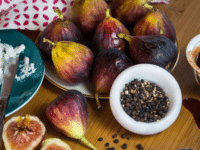 A horizontal image of Stuffed Figs with spoons, a small bowl of whole black pepper, and a bowl of honey.