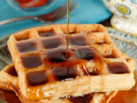 Pouring a syrup on top of two Tahini waffles served on a plate close-up